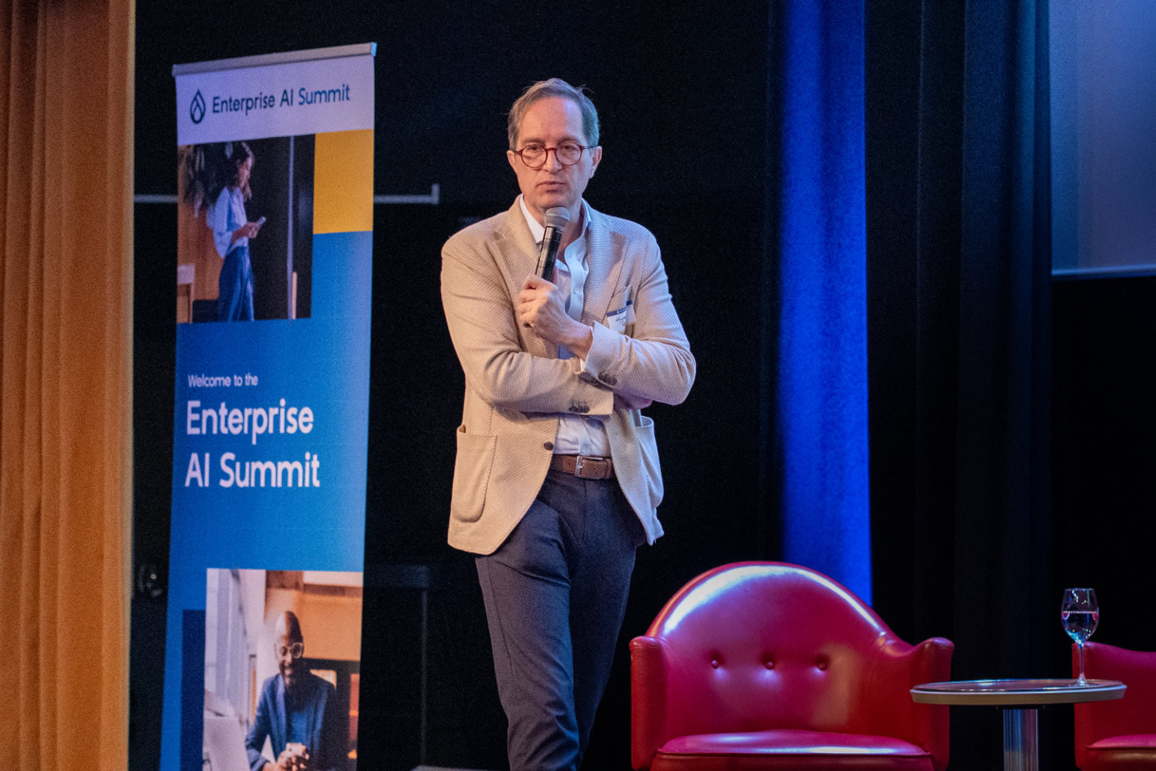 A speaker with a microphone on stage beside the Enterprise AI Summit banner