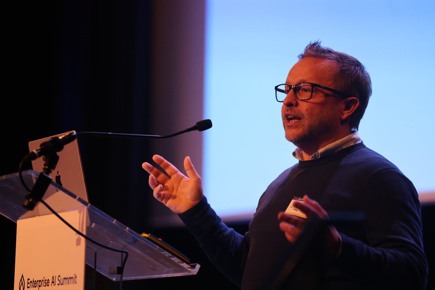A speaker gesturing mid-talk at the Enterprise AI Summit lectern